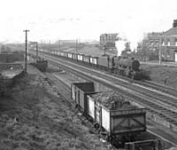 21BKH Another Stanier 8F with a train of ’empties’ travelling from the Bury direction and clearly showing the Permanent Way Bags yard in the background.  B K Hilton.